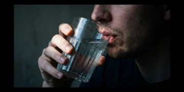 A person taking the first sip from a cold, ribbed glass of water in dramatic chiaroscuro lighting, symbolizing the start of a productive morning routine.