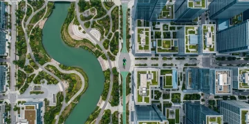 Aerial view of a city park with a winding green river next to modern financial buildings with green rooftops, a person on a green bike path, symbolizing economic resilience.